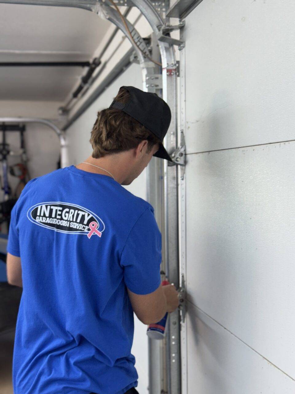 A man in a blue shirt repairs a garage door track in San Jose, CA.